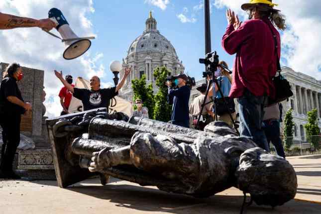 Mike Forcia raises his hands in the air as people photograph the fallen Christopher Columbus statue at the Minnesota state Capitol in St. Paul, Minn., Wednesday, June 10, 2020. Evan Frost, AP